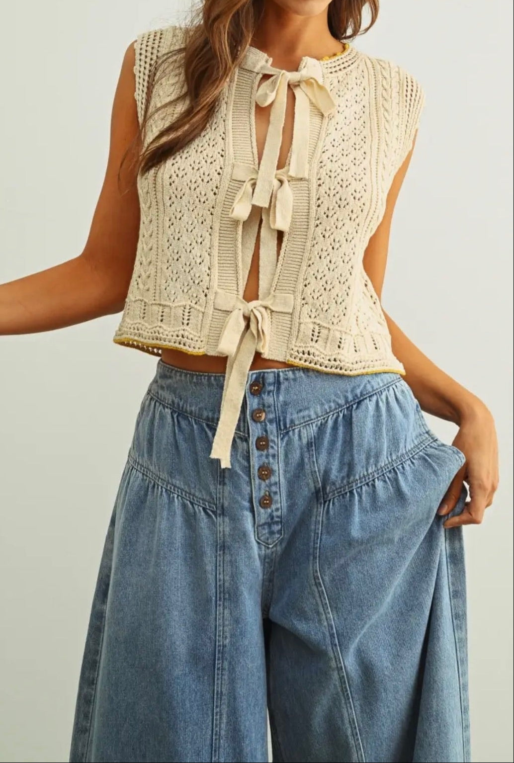 Woman wearing a beige lace top and blue denim pants on a plain background