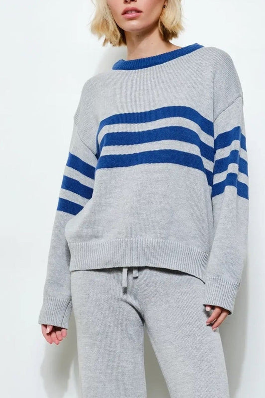 Person wearing a gray sweater with blue stripes and gray pants against a white background