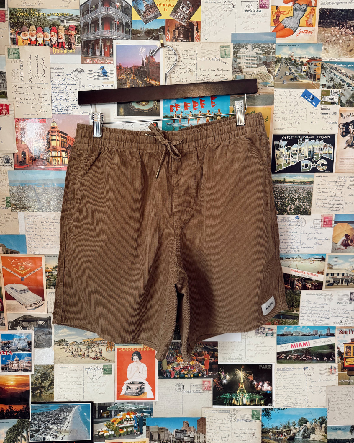 Brown shorts on a hanger against a collage of vintage postcards and photos.