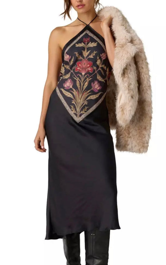 A model wearing a black satin halter midi dress with a large floral embroidered yoke in pink, red, and gold, holding a beige faux fur coat against a white background.